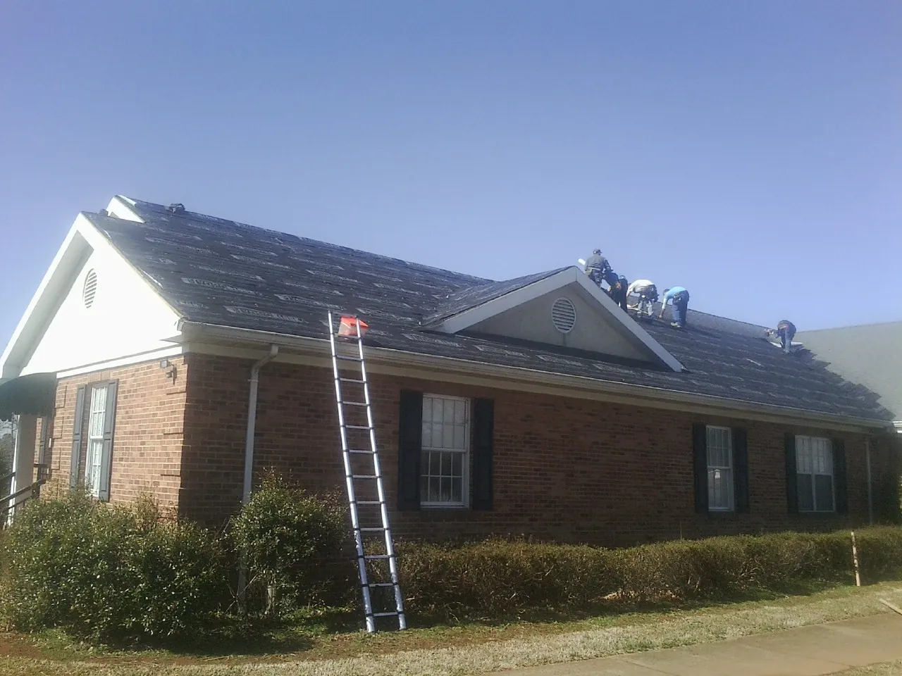 Crew tearing shingles off a brick ranch roof with a ladder set — Emergency Roof Repair work by our crew in Ducktown