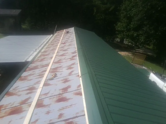 Old rusted panels beside newly installed green metal roofing — Wind Damage Roof Repair by Roofing Brothers in Ducktown