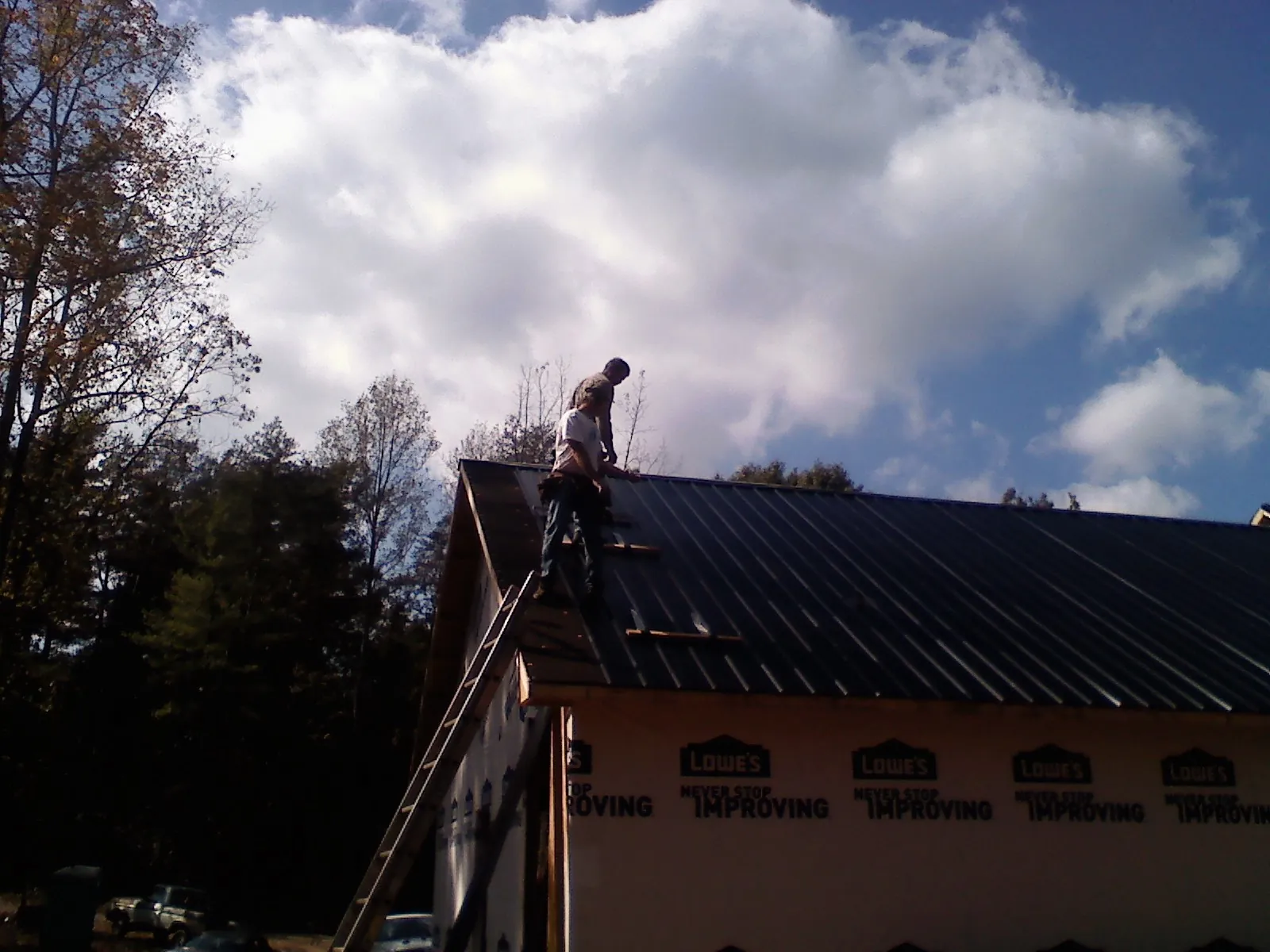 Roofer fastening dark metal panels high against a cloudy sky, from a Roof Inspection job in Ducktown