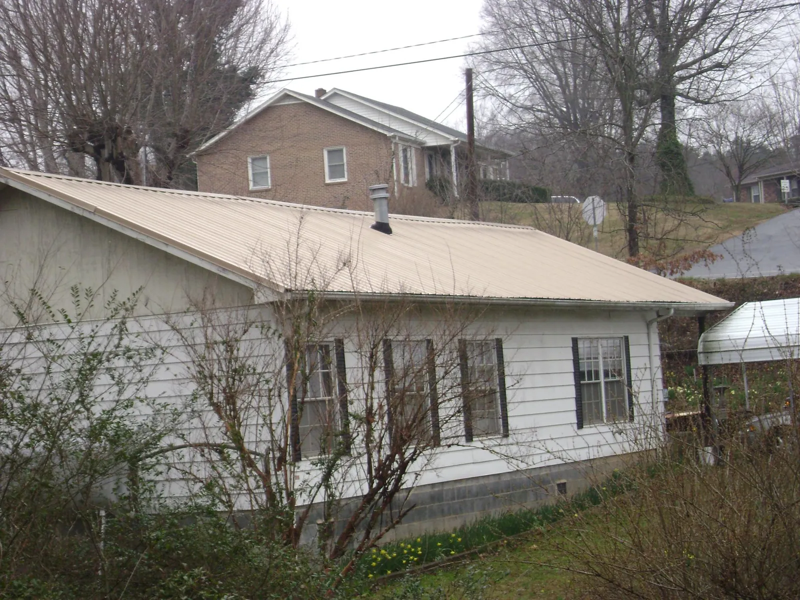 Tan metal roof on a white sided house set into a hillside — Commercial Roofing by Roofing Brothers in Ducktown