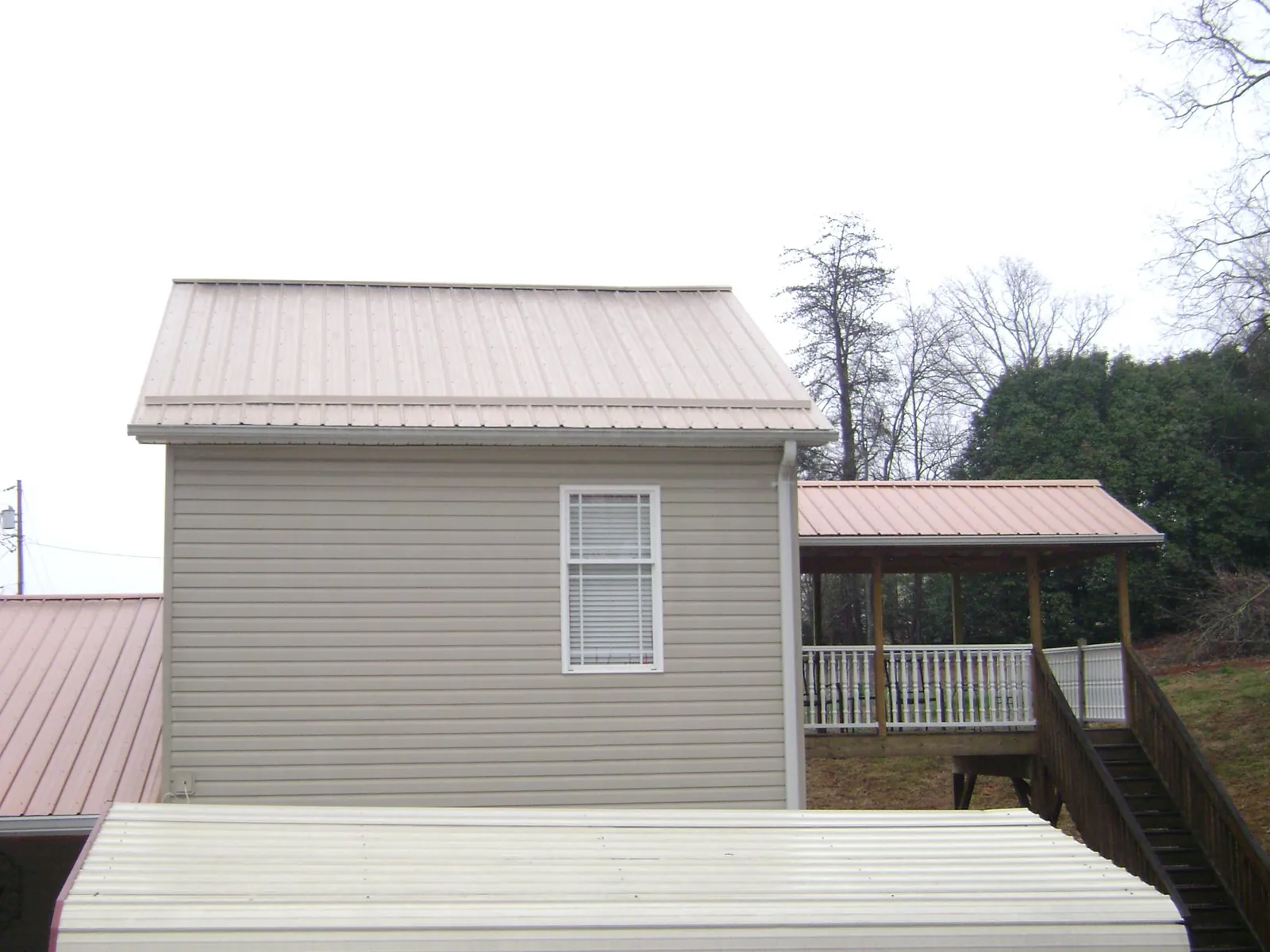 Tan metal roofs on a two story addition and attached porch, from a Roof Replacement job in Ducktown